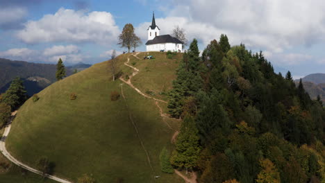 drone hacia la iglesia sveti jakob en la cima de verdes colinas con turistas temprano en la mañana soleada en eslovenia