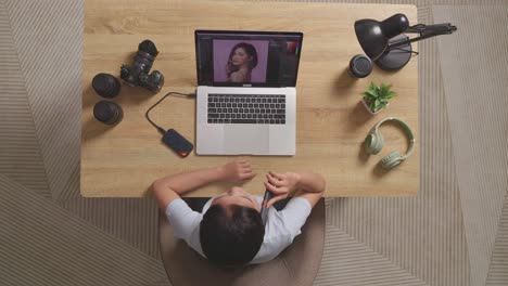 top view of a woman editor talking on smartphone while sitting in the workspace using a laptop next to the camera editing photo of a woman at home