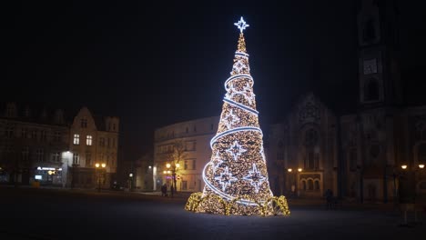large christmas tree full of decorations and lights in a city centre at night