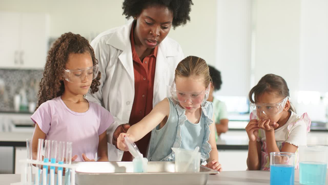 Insegnante afroamericana con camice da laboratorio che guida tre ragazze mentre versano e aggiungono qualcosa in un vassoio di metallo, osservando il colore