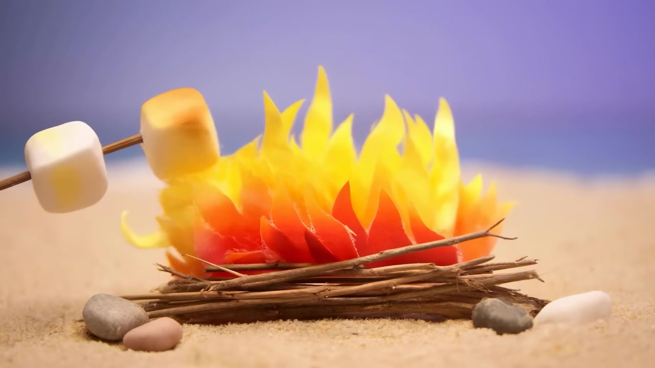 Marshmallow ristes over et miniatyrstrandbål, spiddede marshmallows brunet over utformede papirflammer