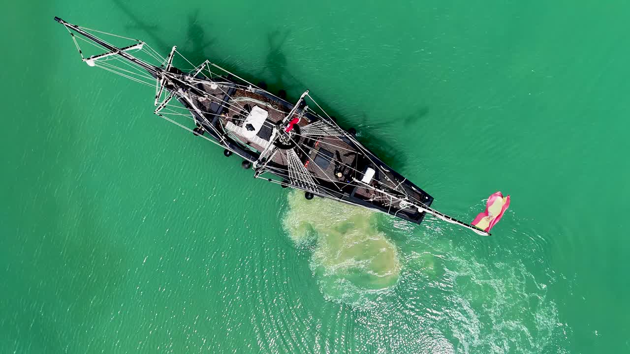 Aerial top-down shot of the historic Nao Victoria arriving in Eastbourne Harbour, with crew members in action and scenic Sussex coastline in view.