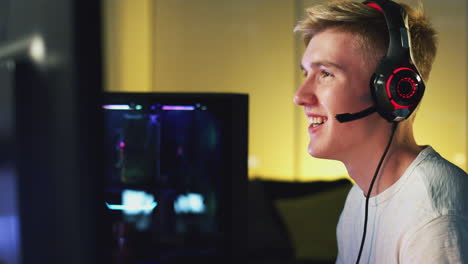 teenage boy wearing headset gaming at home using dual computer screens