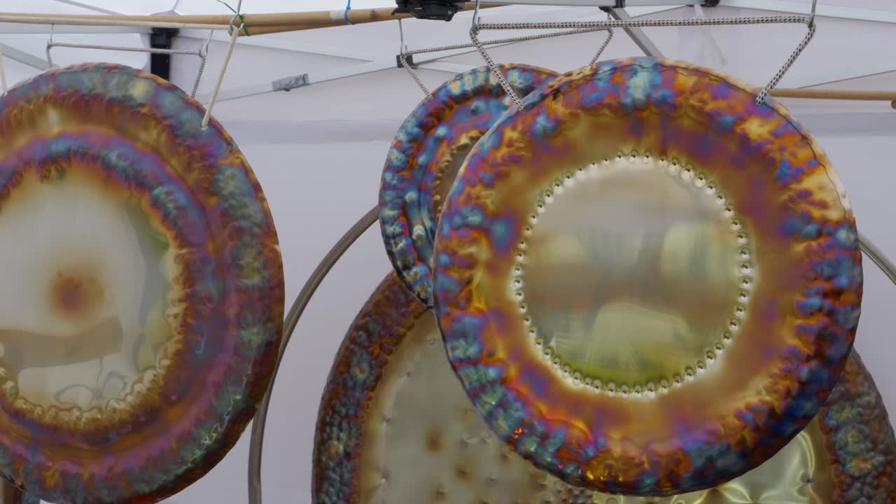 A white mallet strikes a colorful gong. Other gongs can be heard in the background