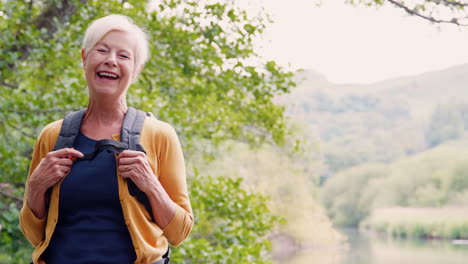 slow motion portrait of laughing senior woman hiking along path by river in uk lake district