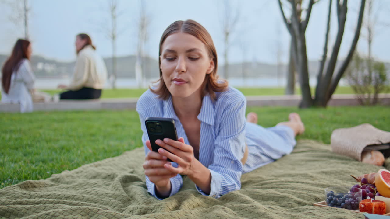 Woman eating grape picnic lying blanket with cellphone closeup. Happy brunette
