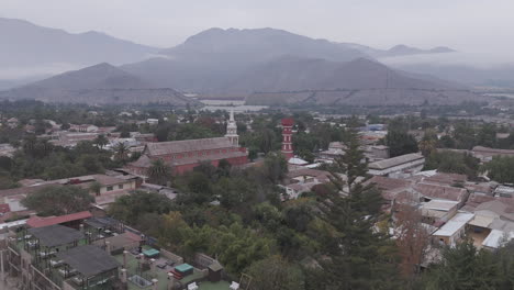 Spiral drone shot around the town of Vicuña near Coquimbo in Chile South America with the main square and red tower Torre Bauer visible on a grey day with mountains in the background LOG
