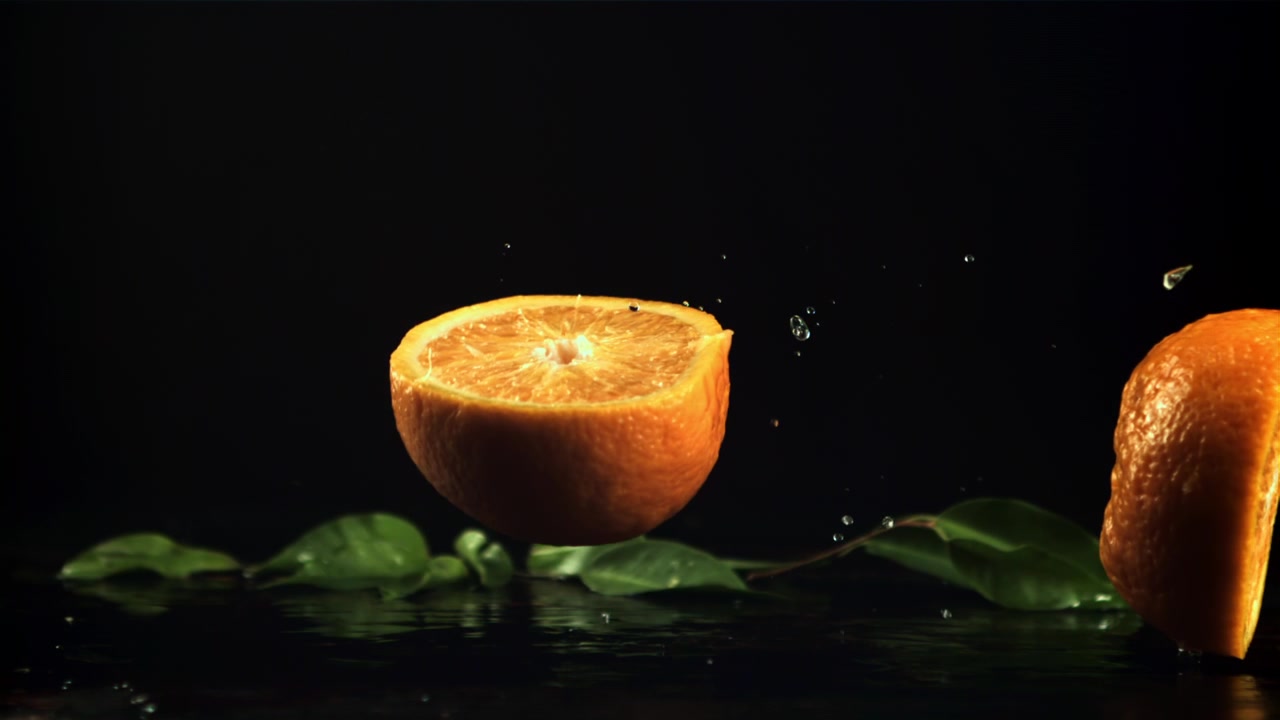 Mezze arance che cadono su una superficie bagnata al rallentatore.