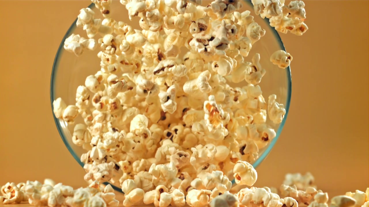 Popcorn, der falder og flyder over fra en glasskål i slowmotion