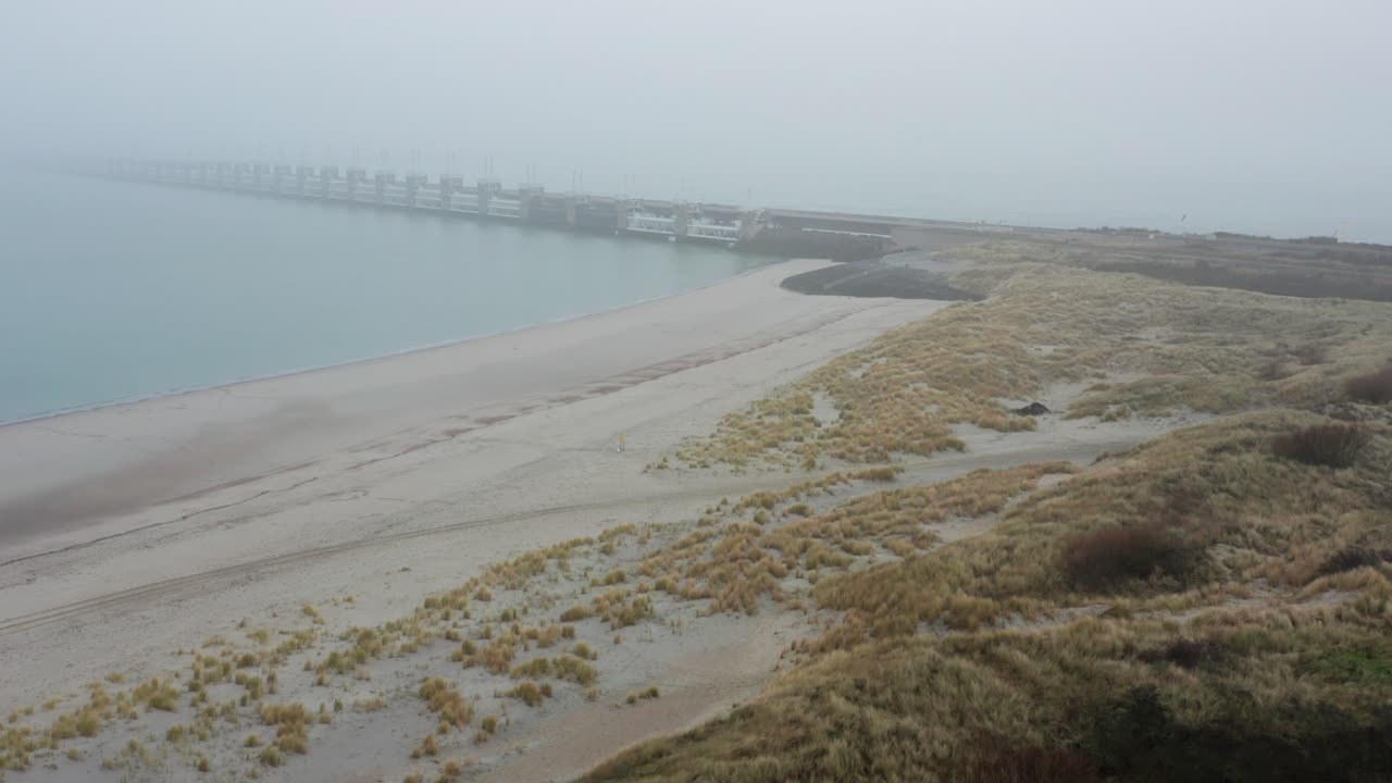 Slow shot of a bridge and storm surge barrier in the Netherlands, during mist. Drone shot
