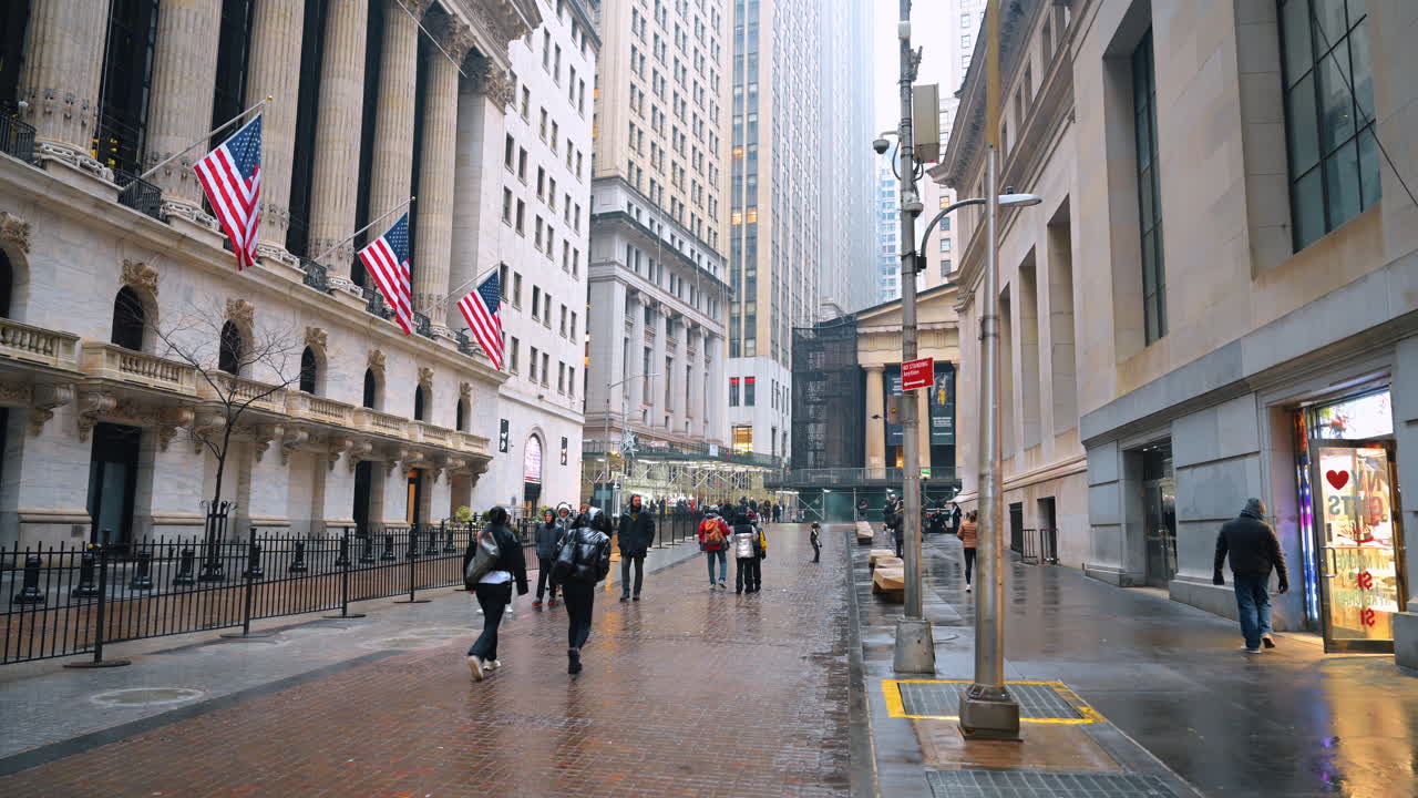 New York, USA, 8. februar 2026: Fodgængere går forbi historisk finansbygning med nationalflag. Bredt skud af Wall Street, der viser børsbygningen med tre amerikanske flag