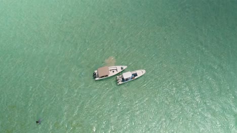 Zenith-view-two-boats-MOORED-in-flat-turquoise-sea-water-WAIT-MEN-kitesurfIng,-Salinas-los-Roques