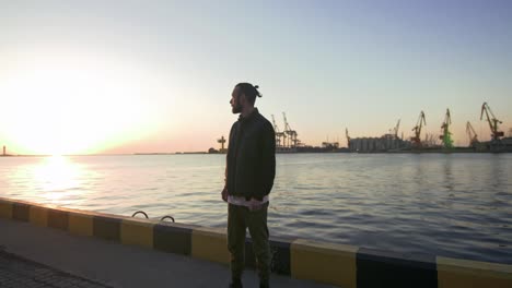 stylish hipster man on sea port background during sunset, looking aside