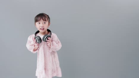 Cute-Asian-girl-with-headphones-enjoys-music-and-dancing,-turning-around-happily-in-the-studio