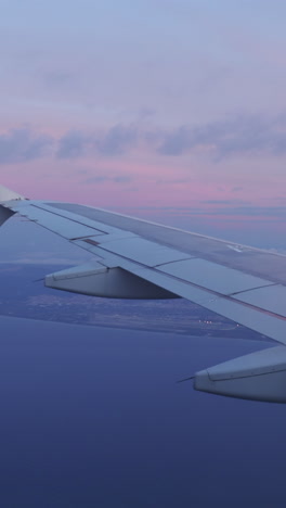 view from a plane window of the sky at sunrise with the wing of the plane in shot in vertical