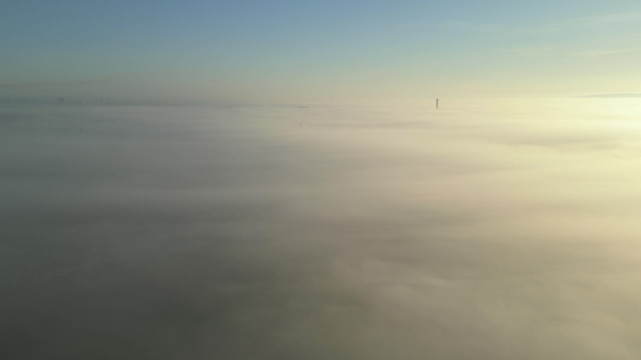A tall chimney rises through dense fog in a peaceful, mist-covered landscape at dawn