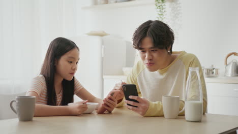father and daughter having breakfast and using a mobile phone