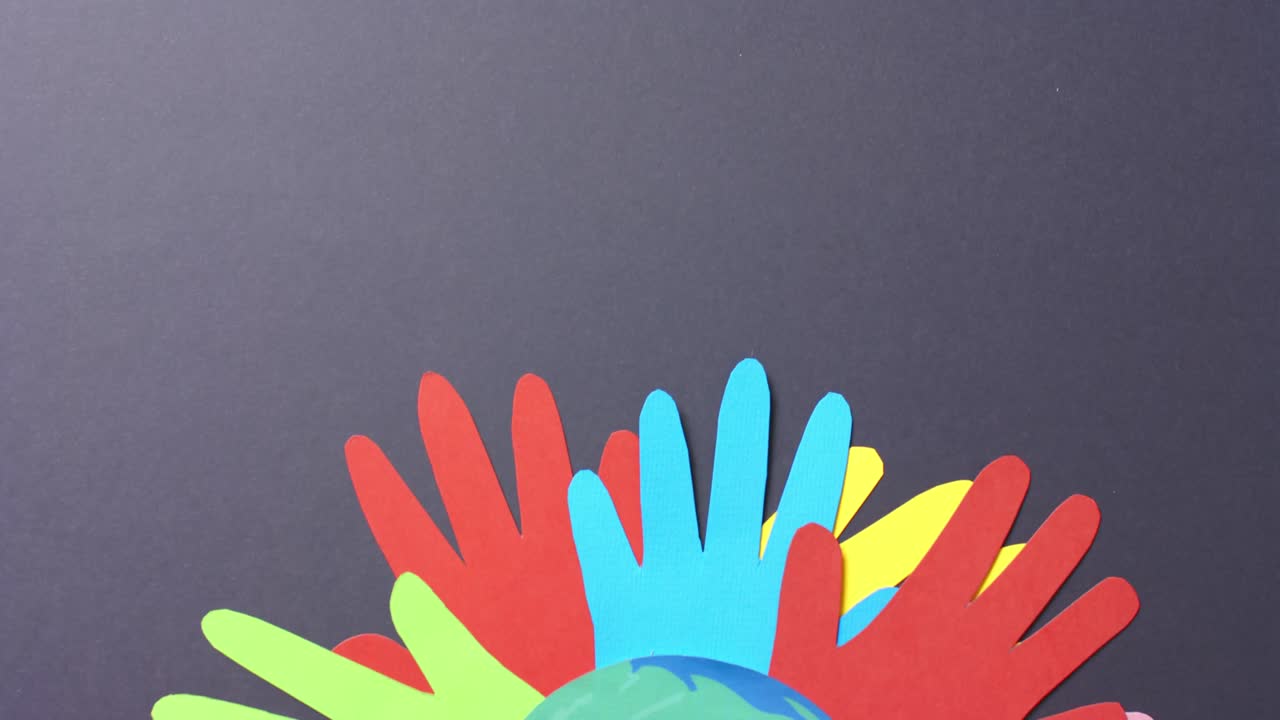 Close up of hands together with globe made of colourful paper on gray background with copy space