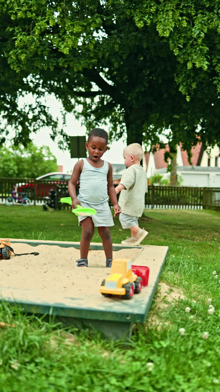 Cute African American boy playing with his best boy friend. Video of cheerful bright European children playing and smiling outside on a summer day. International sandbox game