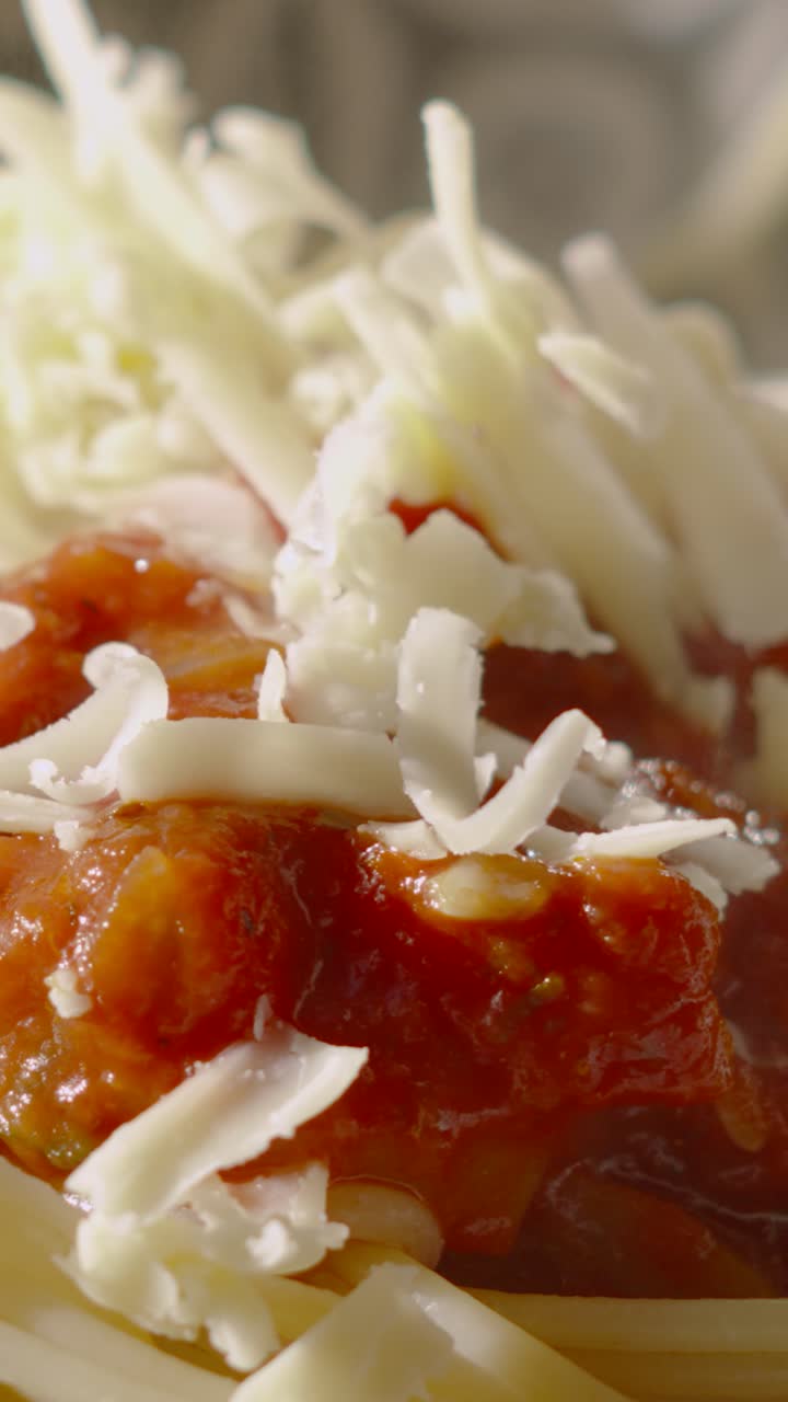 Formaggio che cade al rallentatore, in primo piano, su spaghetti alla bolognese freschi a base di pomodoro. Perfetto per promozioni di ristoranti o documentari culinari. Video verticale in formato 9:16. Ideale per i reels dei social media.