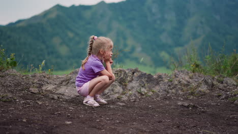 tired girl sits on haunches leaning on palm on rocky hill