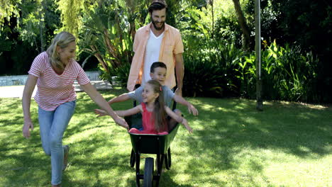 Familia-Feliz-Jugando-Con-La-Carretilla-En-El-Jardín