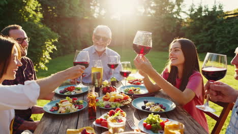 happy multi-generational group enjoying an outdoor dinner and toasting with wine