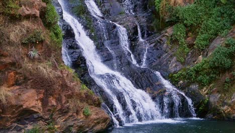 tilt up, slow motion waterfall flowing off rocky mountain into river at walter sisulu national botanical garden, johannesburg, south africa