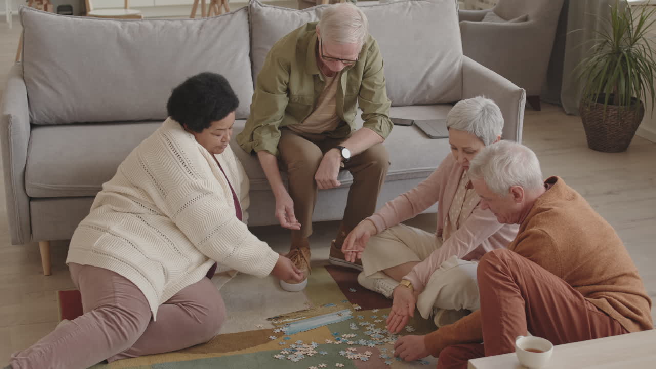 High angle shot of company of diverse senior people sitting on floor, talking, doing puzzle