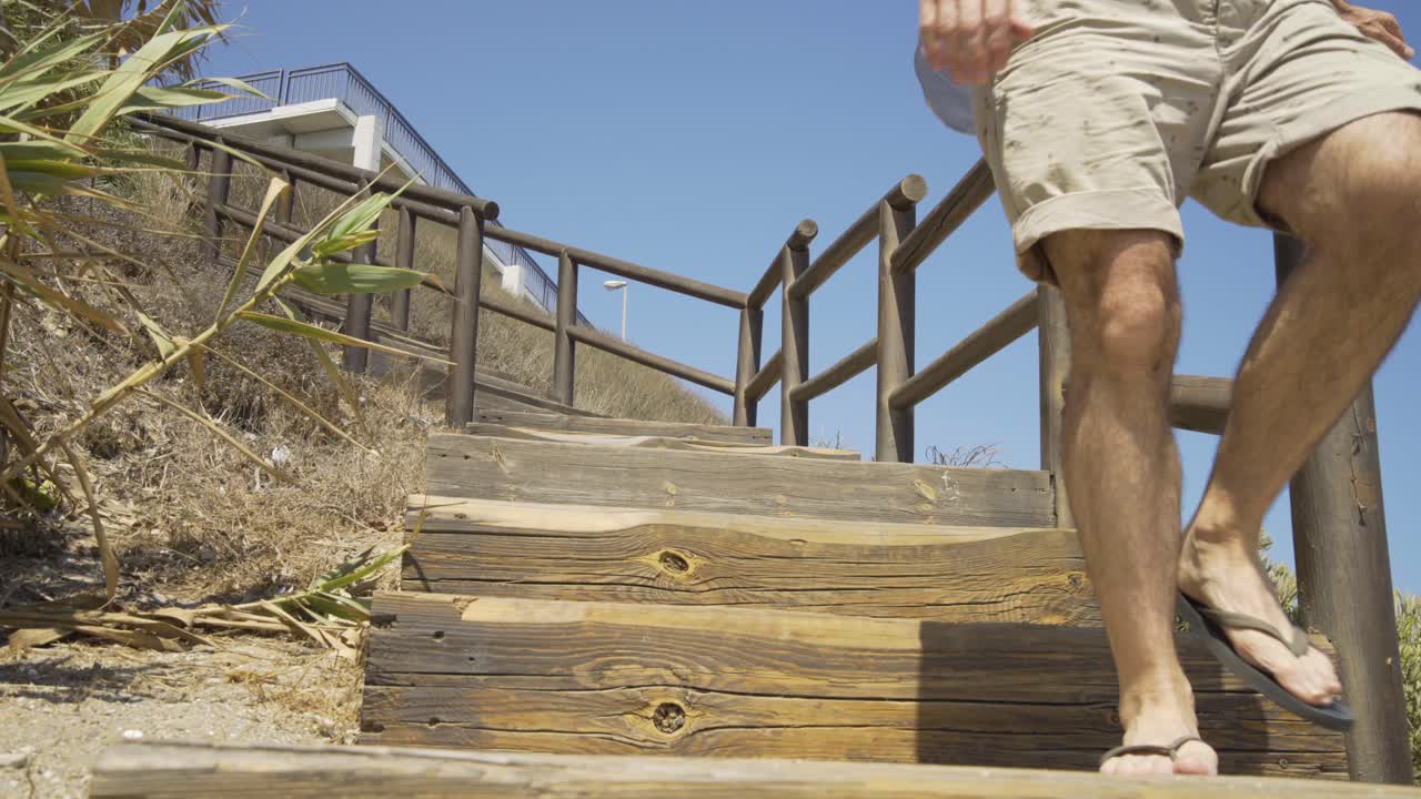 Man Walking down the Wooden steps and onto the beach at Cala de Mijas on the Costa Del Sol in Southern Spain.
