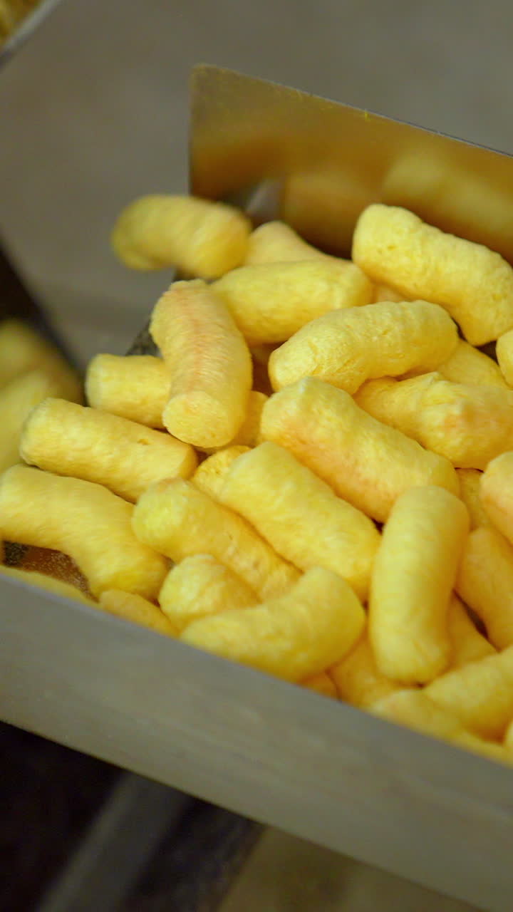 Puffcorn making close up. Sweet golden corn sticks factory. Vertical video