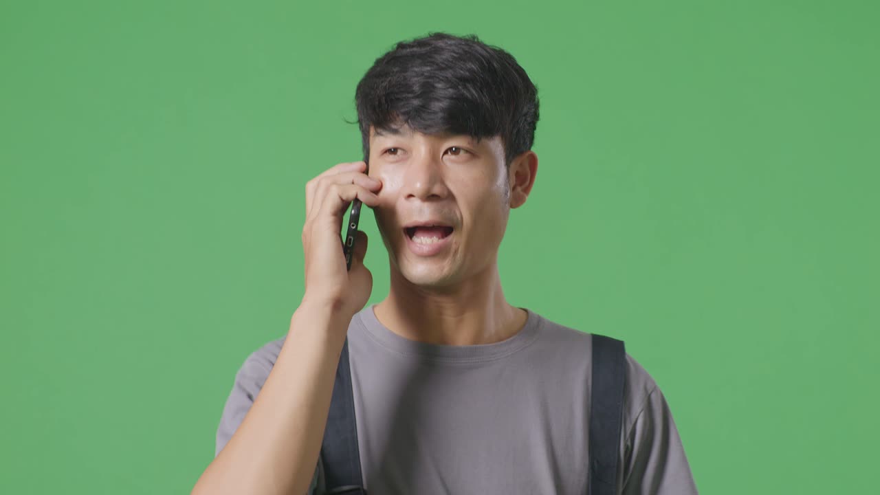 녹색 스크린 배경 스튜디오에서 는 동안 스마트폰으로 대화하고 주변을 둘러보는 아시아 남성 노동자의 클로즈업
