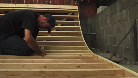 close shot of man with drill building skateboard ramp in his backyard, dolly shot