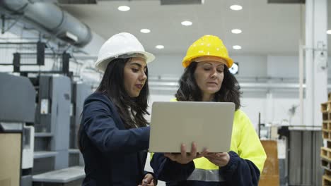 confident female workers standing with laptop at factory