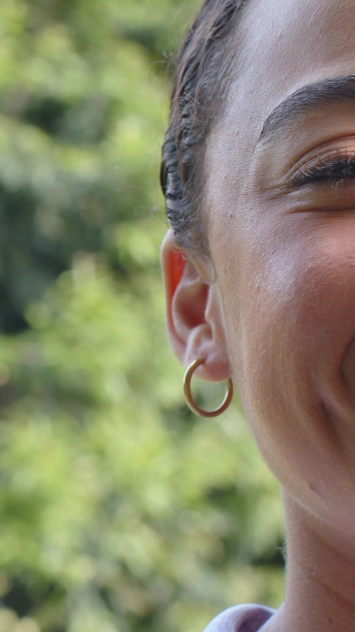 Video verticale: Donna a destra nel parco, testa inclinata, sorridente con top con colletto e orecchino a cerchio d'oro, spazio per il testo