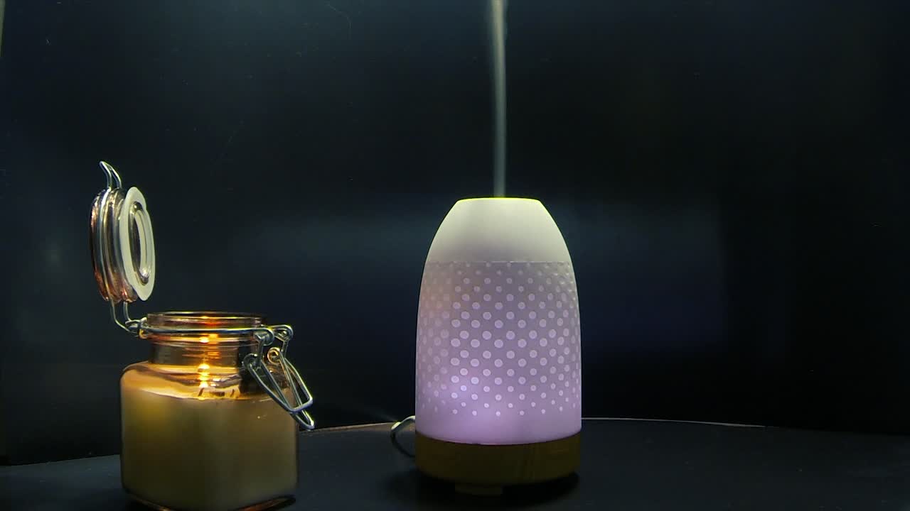 un humidificateur d'air changeant de couleur dispersant une ligne de brouillard à côté d'une bougie de flamme allumée dans un pot en verre
