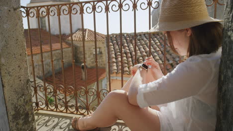 woman using smart watch checking messages browsing enjoying warm sunny day on vacation sitting on balcony happy tourist relaxing wearing hat in italy