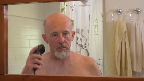 caucasian male using electrical trimmer to cut his hair and beard