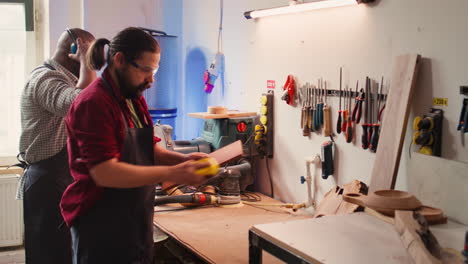 Handwerker-Neben-Einem-Kollegen,-Der-Mit-Einem-Schleifblock-Unebenheiten-Aus-Holz-Entfernt