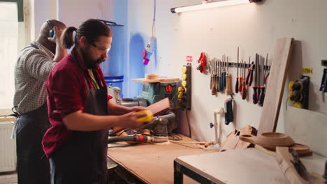 artesano al lado de un compañero de trabajo usando un bloque de lijado para eliminar las imperfecciones en la madera
