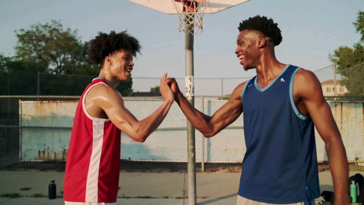 Jumping two players wearing red and blue jerseys after rebound under park hoop, sharing fist bump