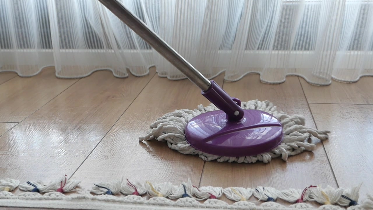 A purple mop cleaning a wooden floor in a bright room