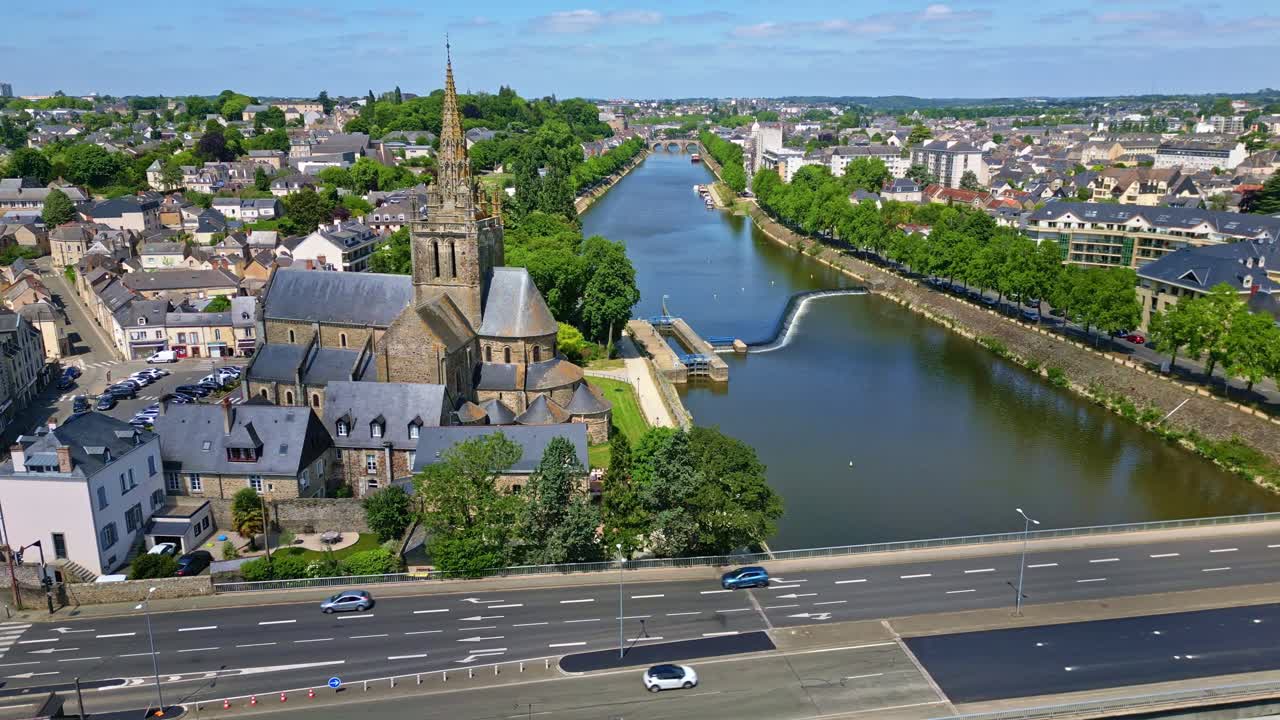 Drone flies laterally past Notre-Dame d'Avesnières, showing Mayenne River, road, and surrounding Laval cityscape with light traffic - France