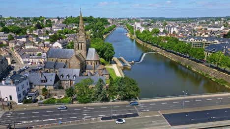 drone flies laterally past notre-dame d'avesnières, showing mayenne river, road, and surrounding laval cityscape with light traffic - france