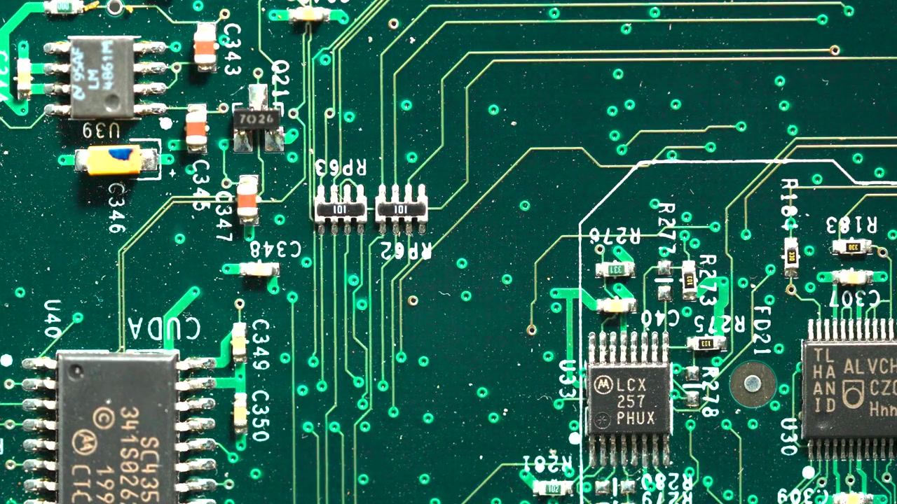 High angle detailed shot of a green computer motherboard showing transistors and integrated circuits.