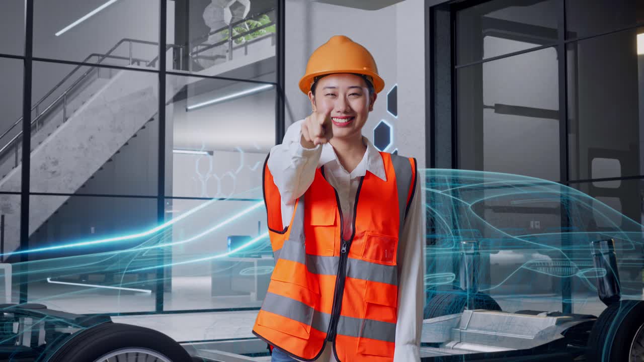 안전 헬을 입은 아시아 여성 엔지니어가 웃으며 가을 만지고 전기 차량의 개념을 가지고 서있는 동안 당신을 가리키고 있습니다.