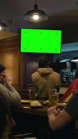 Vertical-shot-of-African-American-fan-celebrating-with-friends-when-football-team-scores-goal-and-wins-the-tournament.-Group-of-multicultural-friends-watch-live-soccer-match-sitting-in-sports-bar-or-pub.