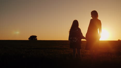 a woman with a girl admires the beautiful sunset in a picturesque place silhouettes of mom and daugh