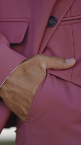 stylish man wearing pink tuxedo puts hand into pocket resting in spring park closeup slow motion. businessman spends time relaxing in garden