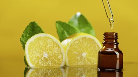 dripping lemon juice from pipette into bottle close-up, vitamin oil. making aroma serum on yellow background. dropping liquid citrus extract, skincare routine, treatment spa. traditional medicine